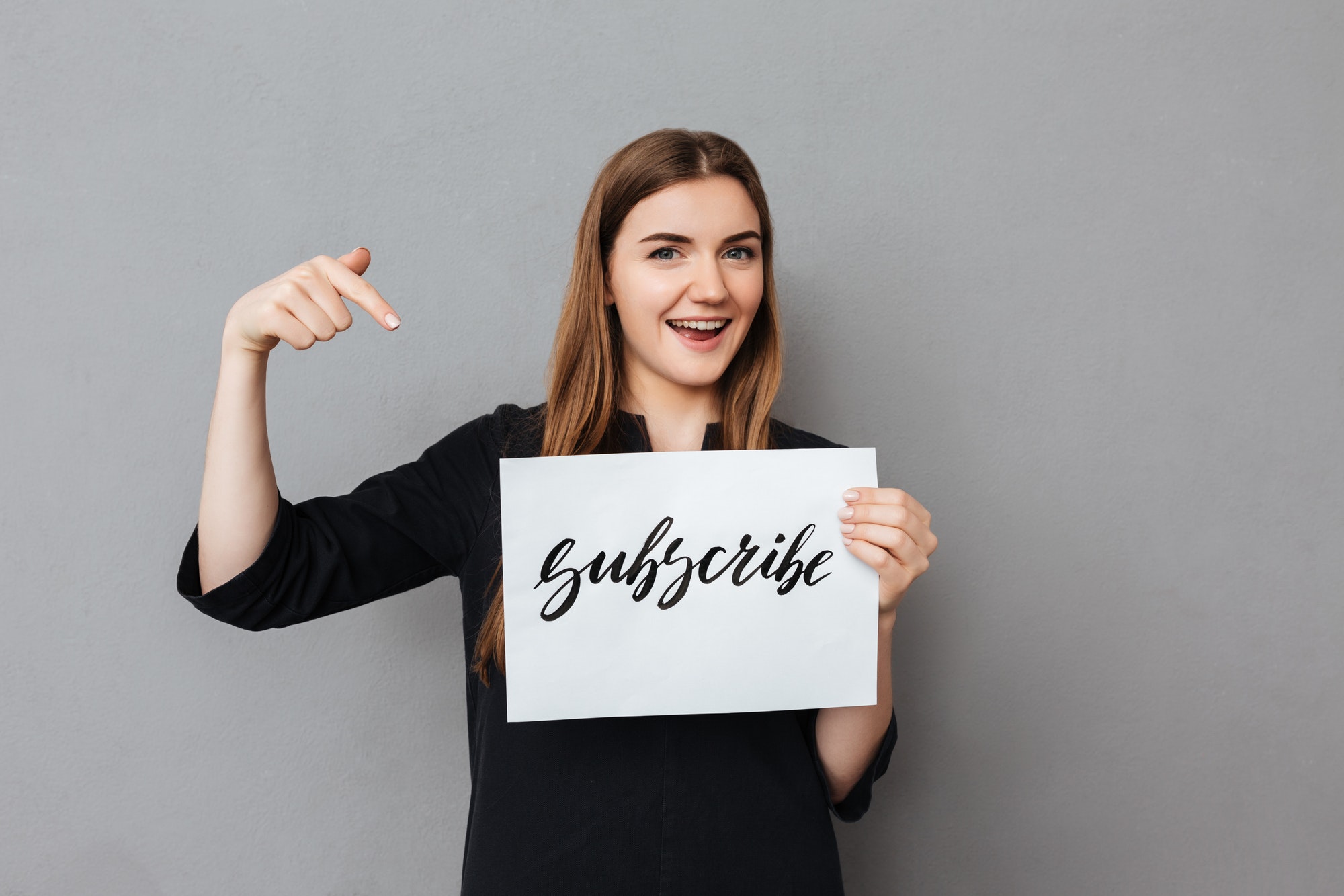 Portrait of beautiful smiling girl standing and holding postcard on gray background